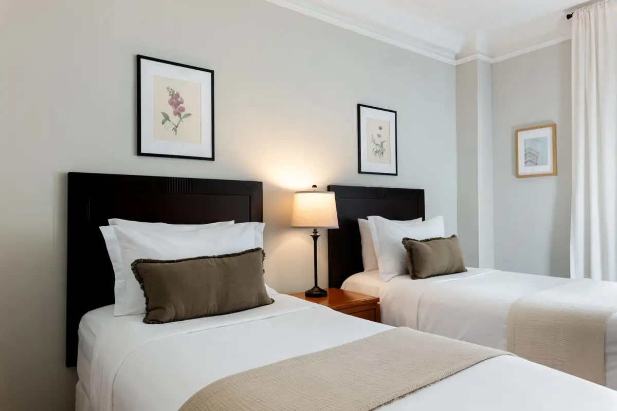 Bedroom with two twin beds with dark headboards, olive and beige pillows and a lamp between the beds.
