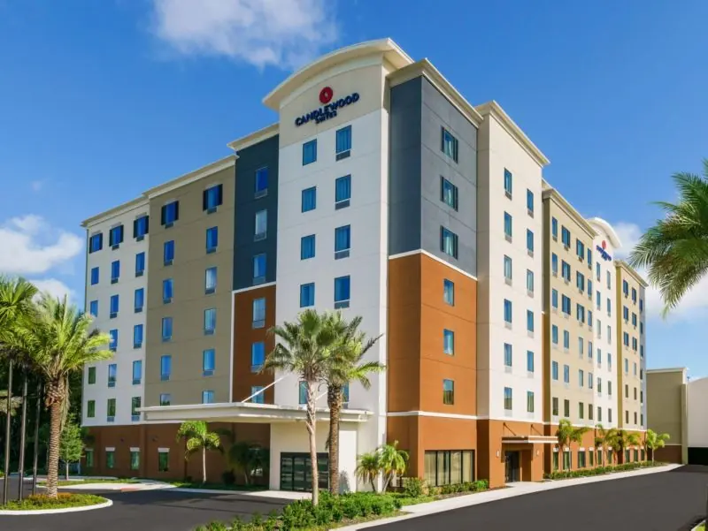 Multi-story hotel building with palm trees and a driveway under a blue sky.