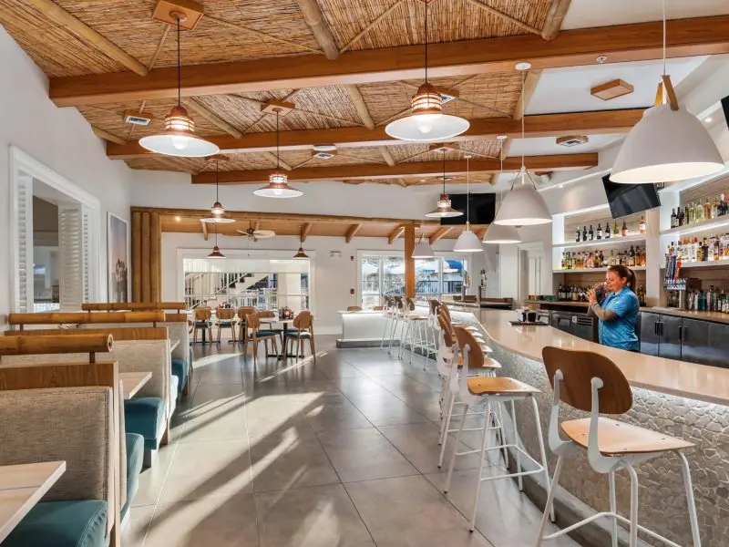 Restaurant with bar stools, booths and pendant lamps under a wood-beam ceiling.