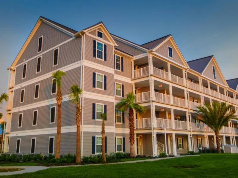 Multi-story building with balconies, palm trees and a lawn.