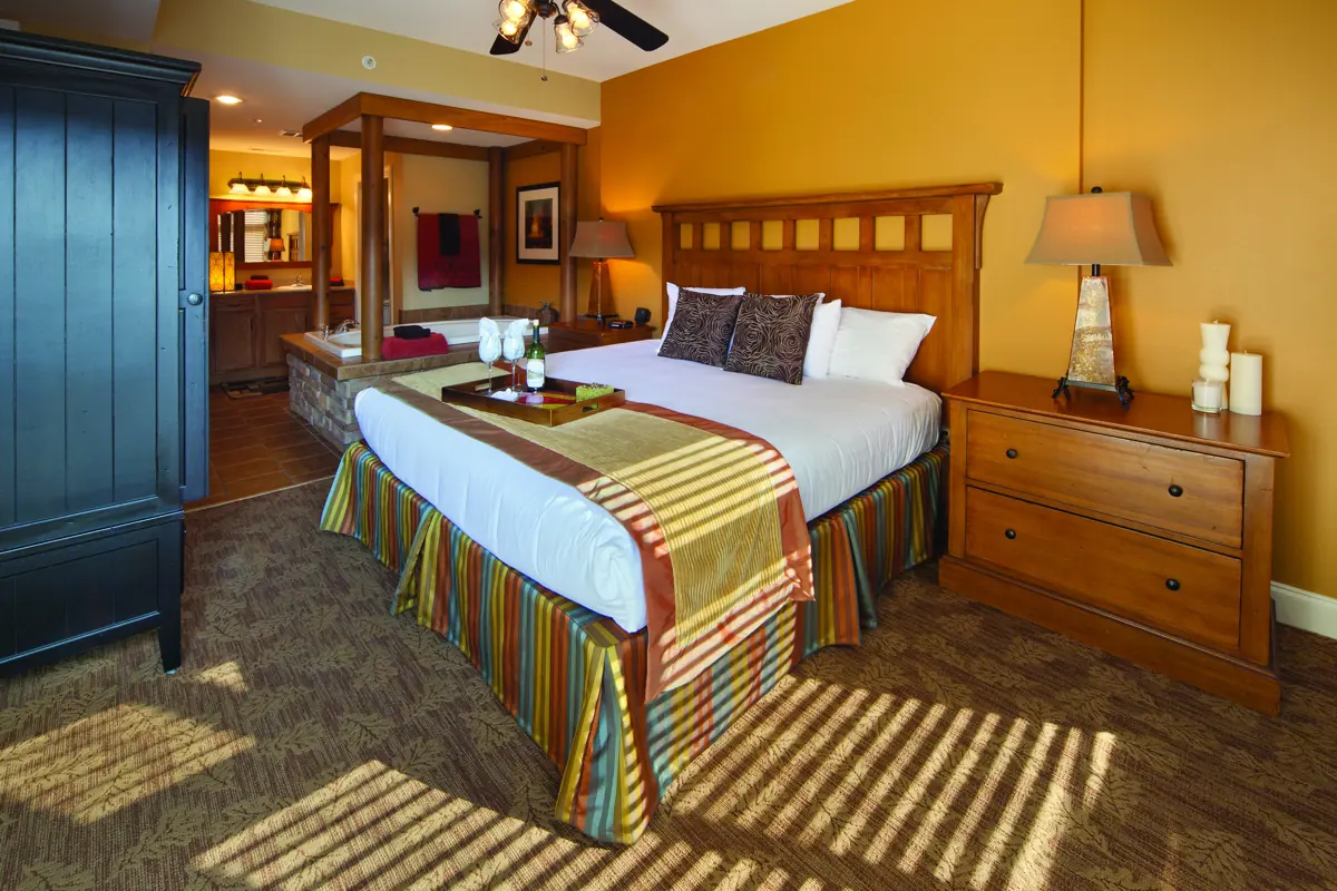Similar room (illustrative): bedroom with a bed with a striped runner, wooden headboard, nightstand lamp and a dark armoire.