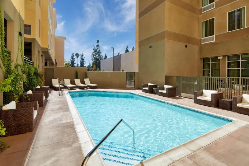 Outdoor swimming pool with loungers and seating, surrounded by hotel buildings.