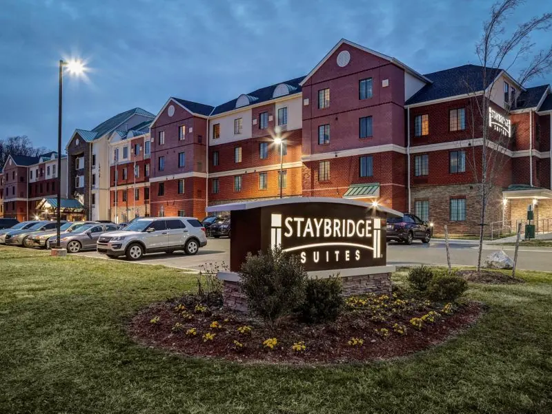 Brick hotel buildings at dusk behind a Staybridge Suites sign in a flower bed.