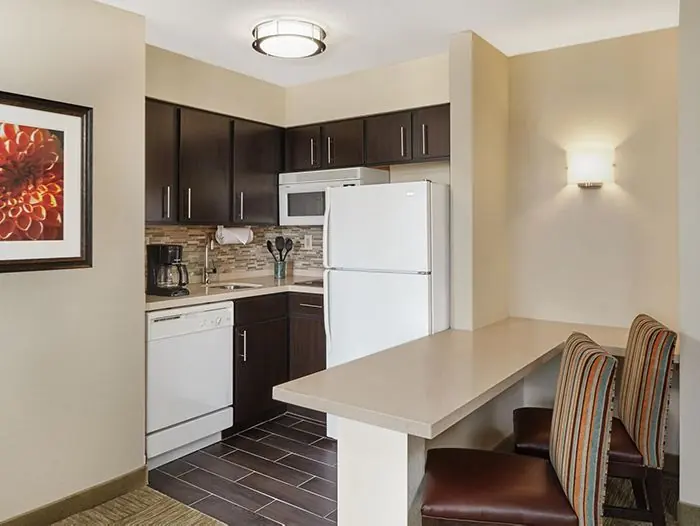 Kitchen with white refrigerator, dishwasher and microwave, dark cabinets, and a breakfast bar with two striped stools.
