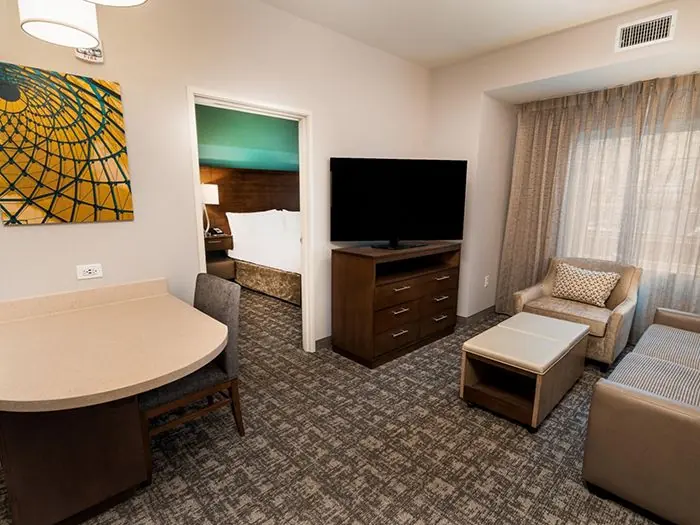Living area with armchair, TV and table, open door to bedroom.