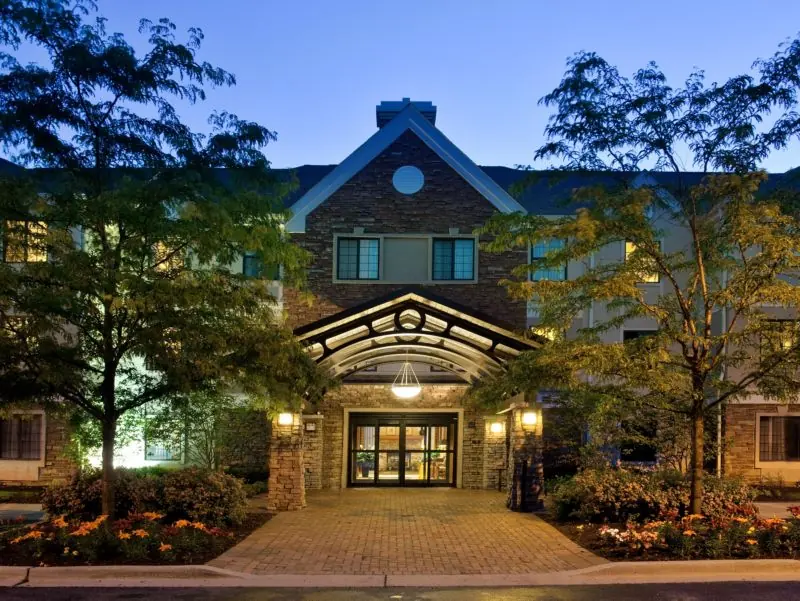 Hotel entrance with a covered canopy among trees, with lit windows.