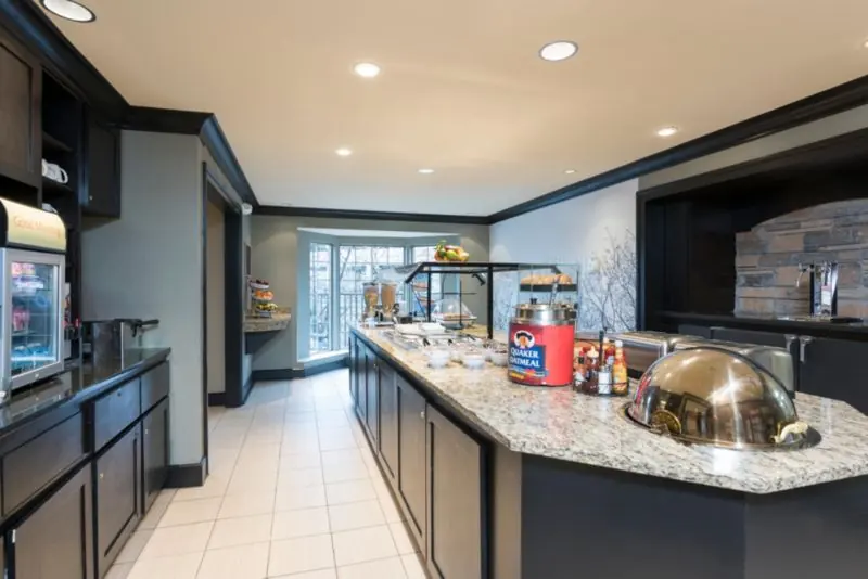 Breakfast counter with a granite top, a covered serving dish and cereal and drink dispensers.