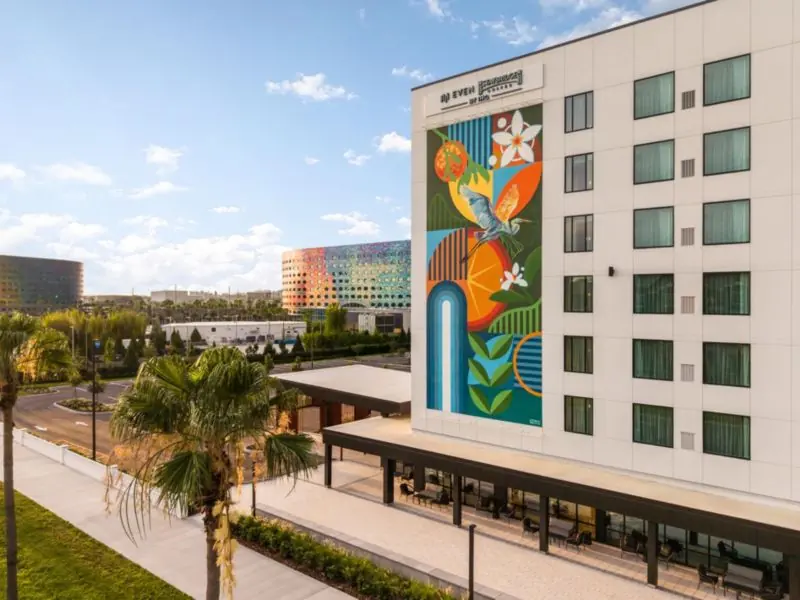 Hotel building with a large colourful mural on its side and a palm tree in front.